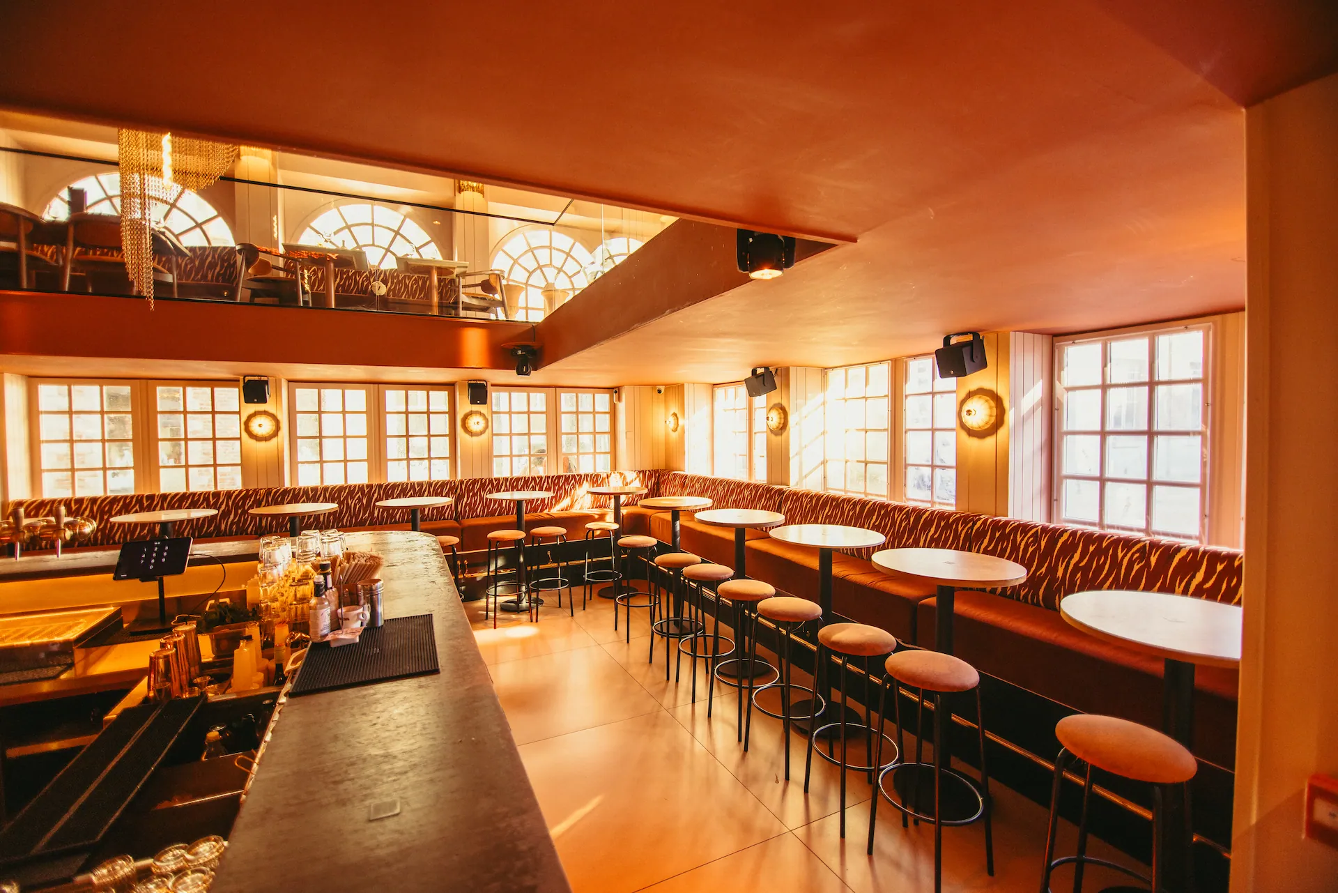 Le long comptoir du bar face aux rangées de tables hautes, sous la mezzanine et ses fenêtres cintrées