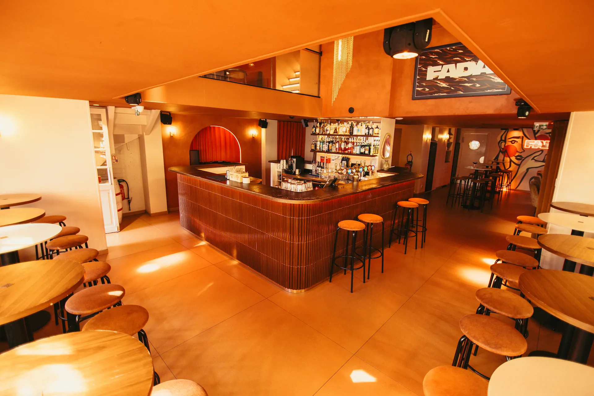 Le comptoir arrondi et ses tabourets orange, les bouteilles alignées sur les étagères derrière