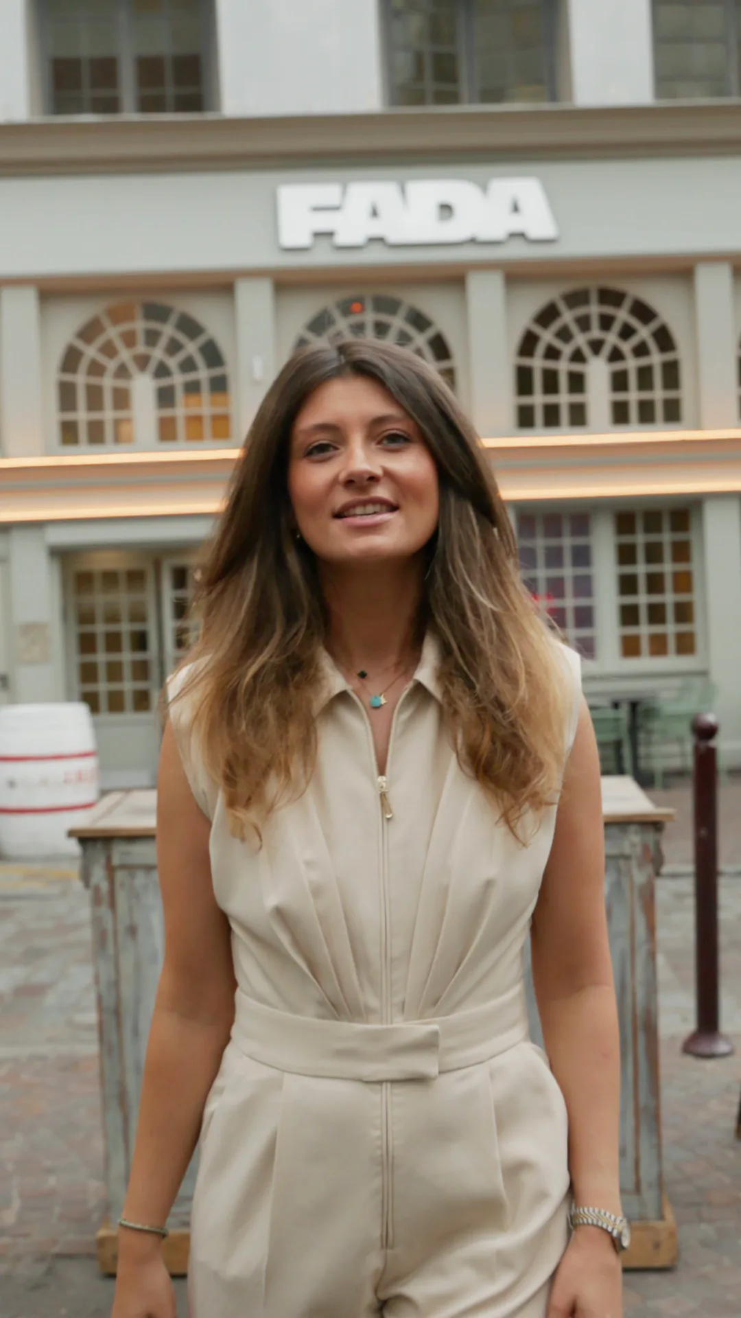 Une femme sourit face à l'objectif devant la façade du FADA, son enseigne au-dessus des fenêtres cintrées