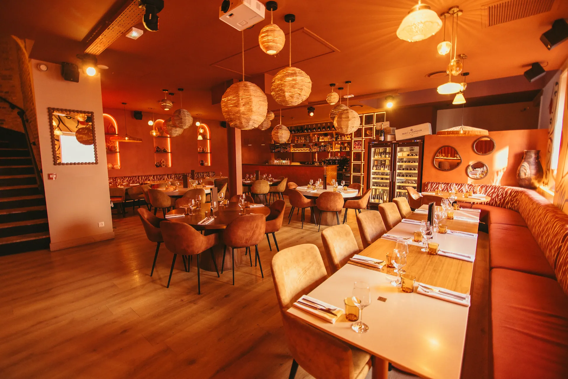La grande salle du restaurant, une longue tablée le long d'une banquette sous des suspensions en osier, les caves à vin au fond