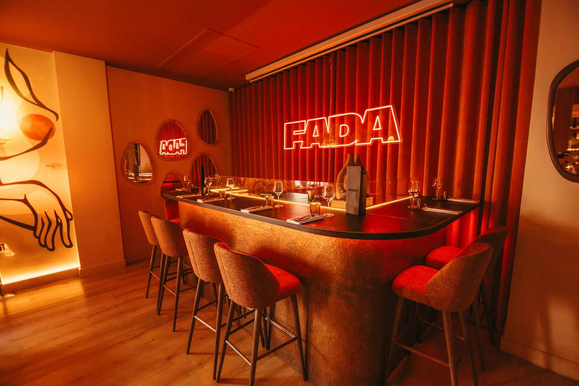 Un petit comptoir et ses tabourets hauts devant un rideau rouge et l'enseigne néon FADA